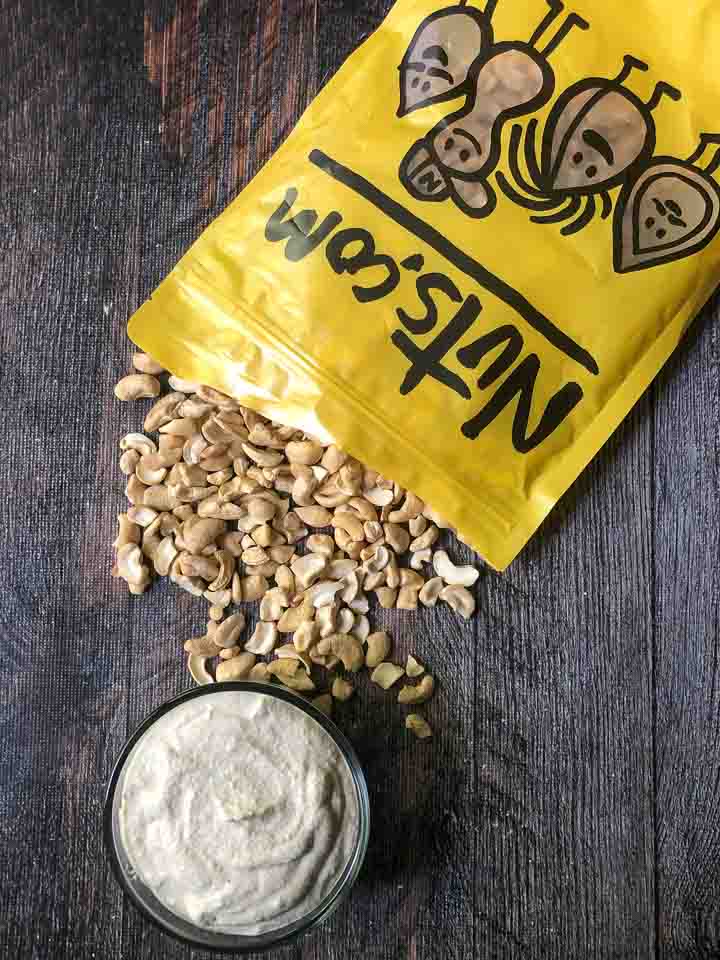 yellow bag of raw cashews spilling out and a glass bowl with cashew cream cheese