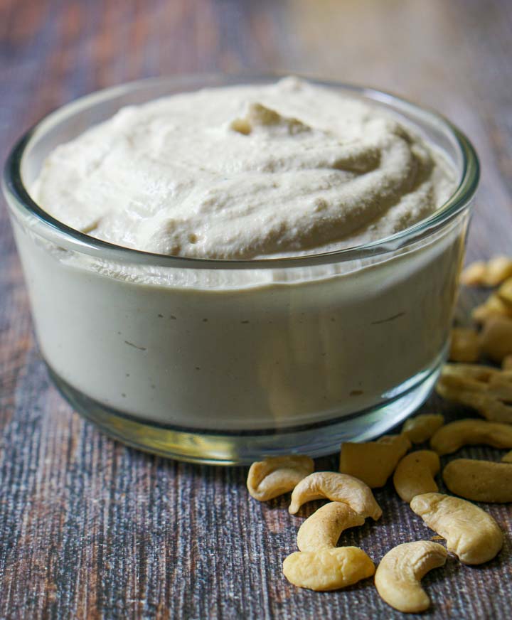 closeup of a glass bowl with low carb cashew cream cheese and scattered cashews
