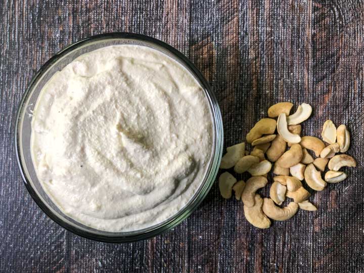 aerial view of a glass bowl with low carb cashew cream cheese and scattered cashews