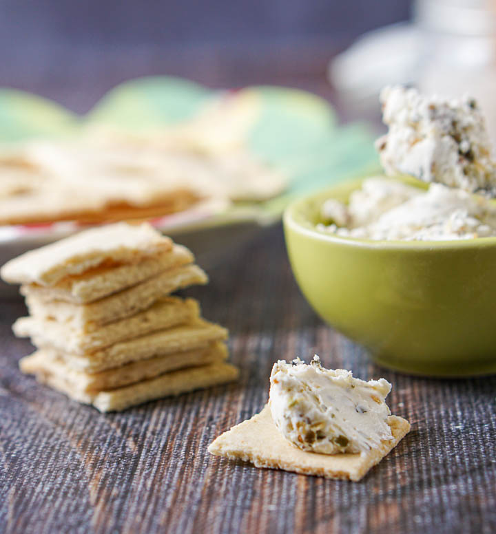 closeup of a stack of almond thin crackers and one with the spread on it. 