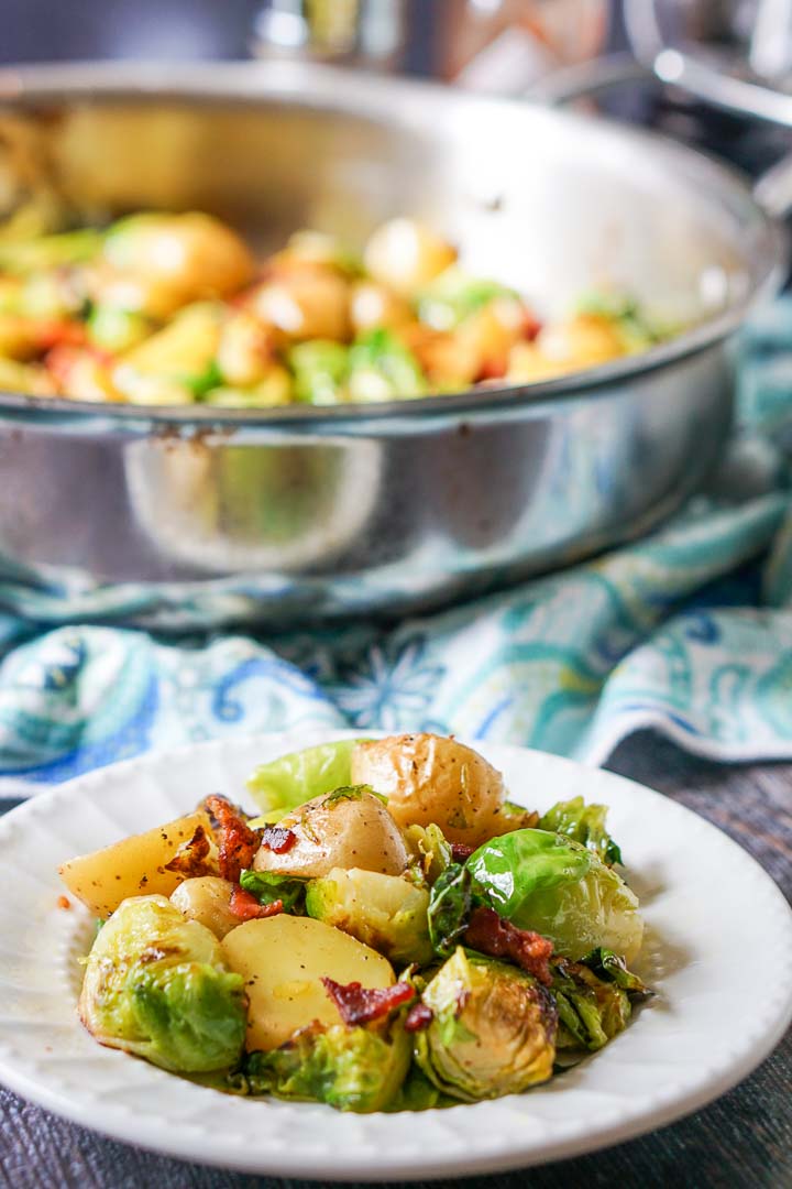 white plate with Brussels sprouts & potatoes side dish and pan in background