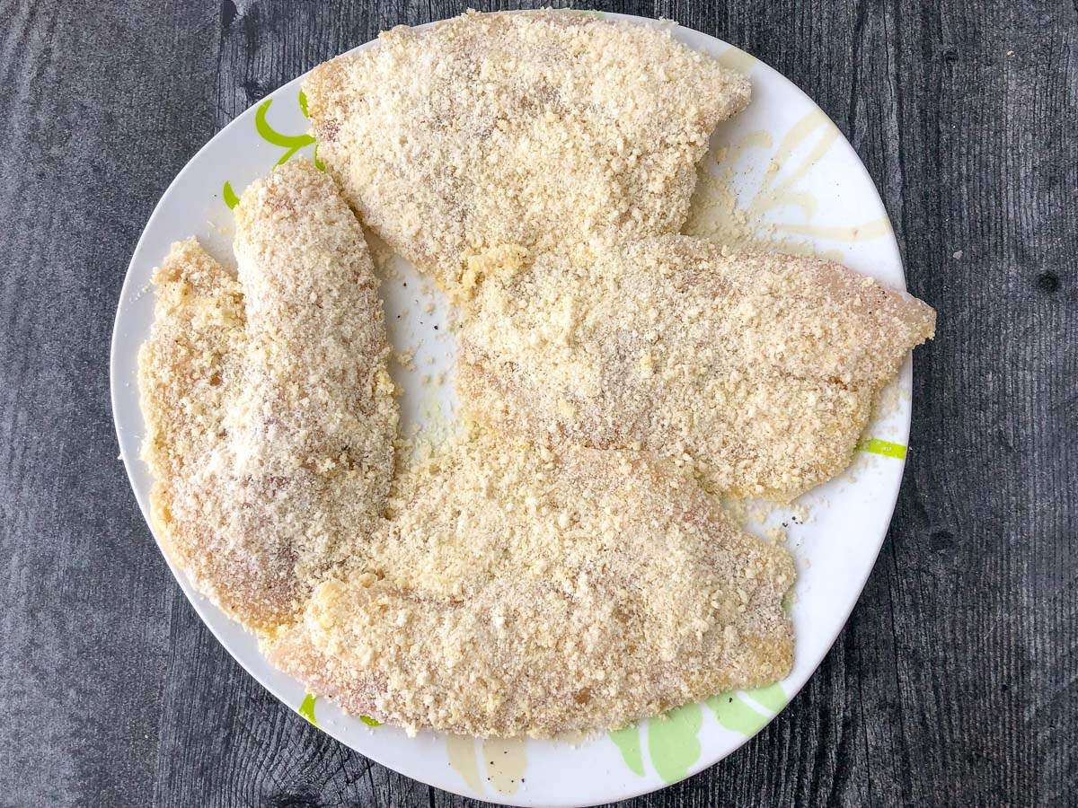 breaded raw tilapia on a white plate