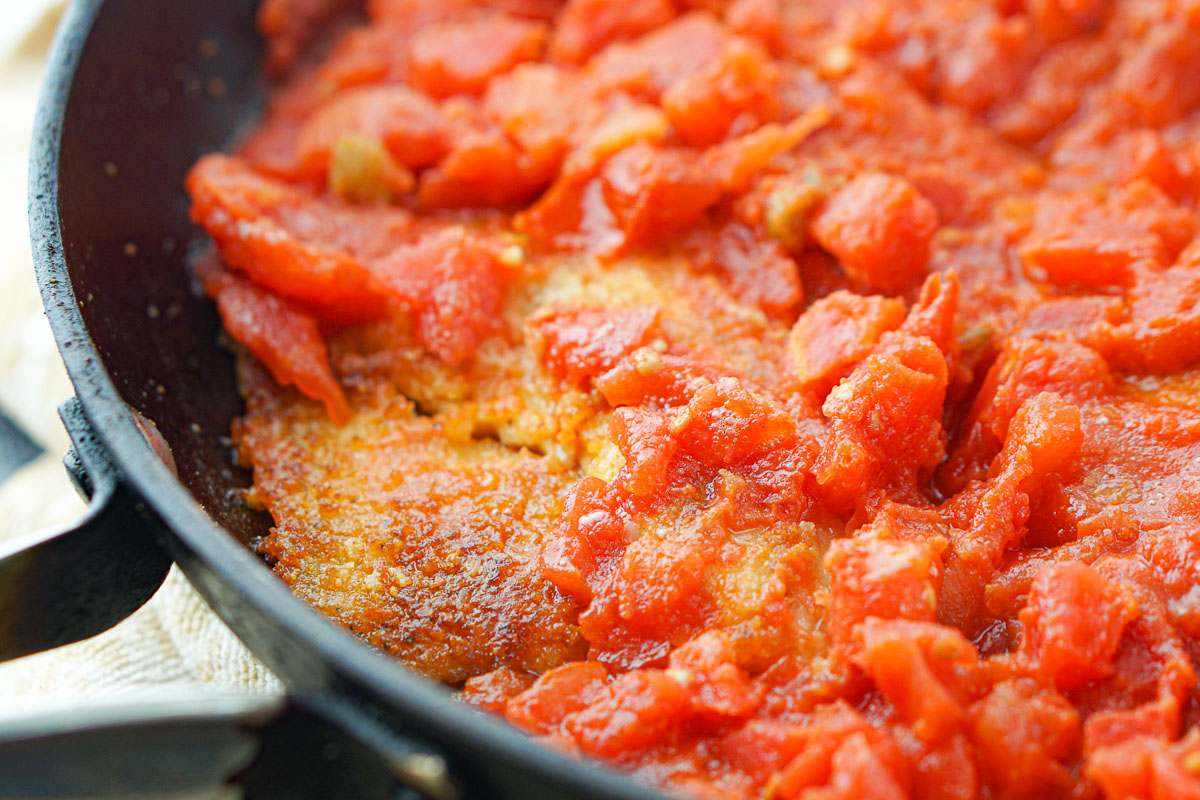 closeup of a pan of breaded pan fried tilapia and tomatoes