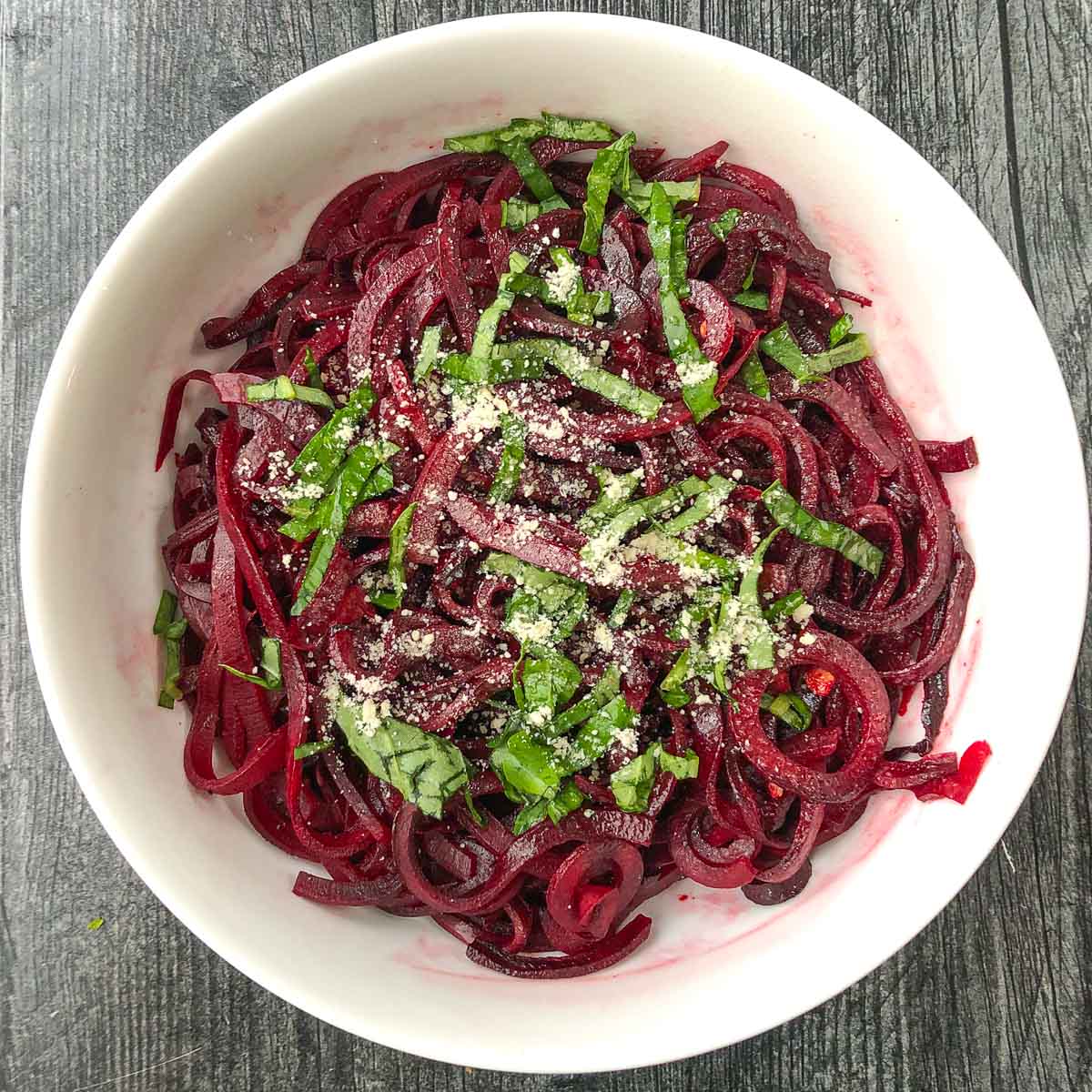 white bowl with beet noodles and fresh basil 