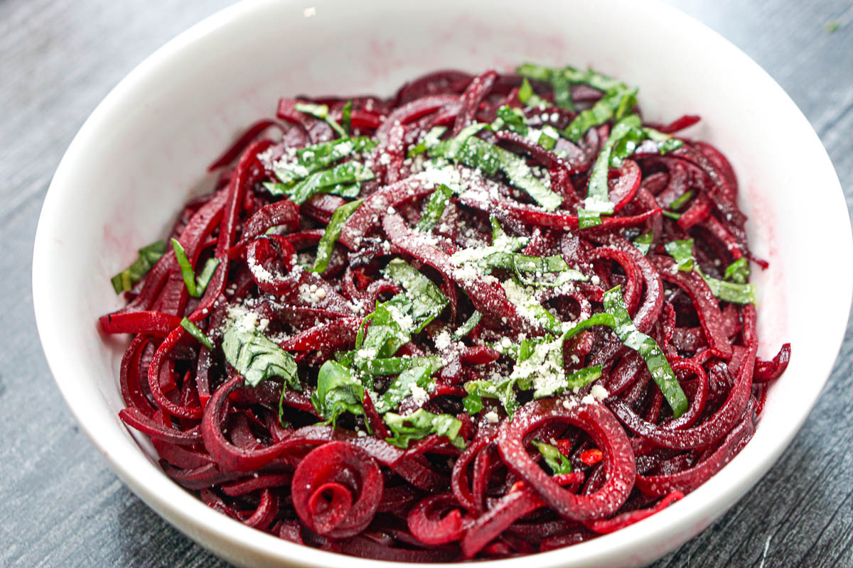 closeup of a bowl of beet noodle pasta with fresh basil and parmesan cheese