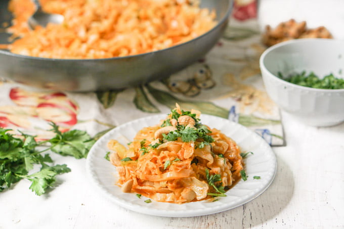 white plate with red curry cabbage noodles and a pan in the background