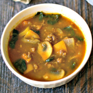 White bowl with easy paleo pumpkin soup with sausage and kale.