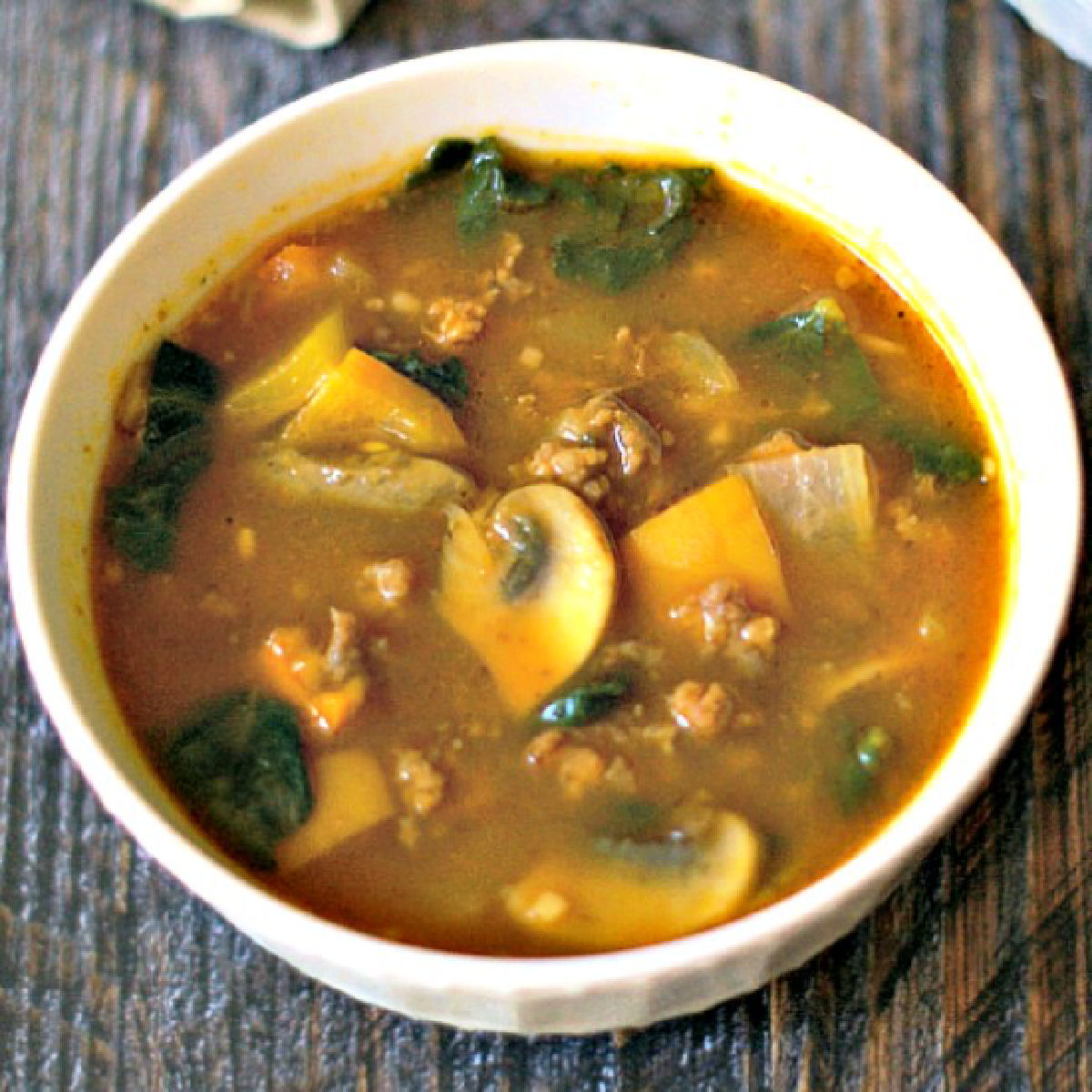 White bowl with easy paleo pumpkin soup with sausage and kale.