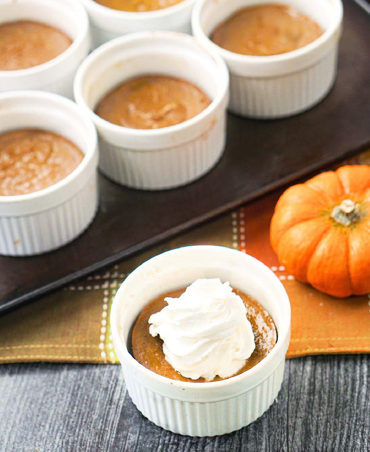 baking sheet with 5 dessert dishes with keto pumpkin pie and one with whipped cream and a mini pumpkin