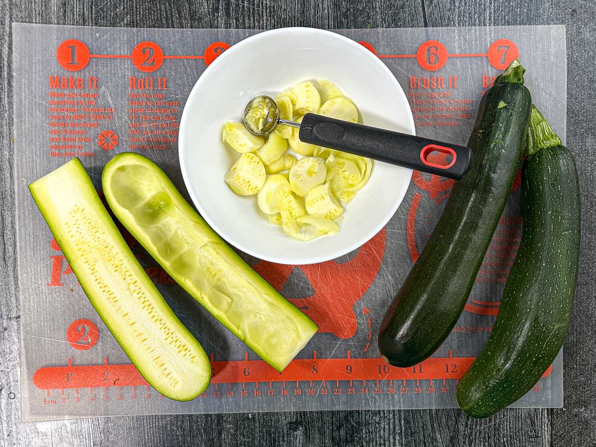 Raw zucchini halves with a scooper cleaning it out.
