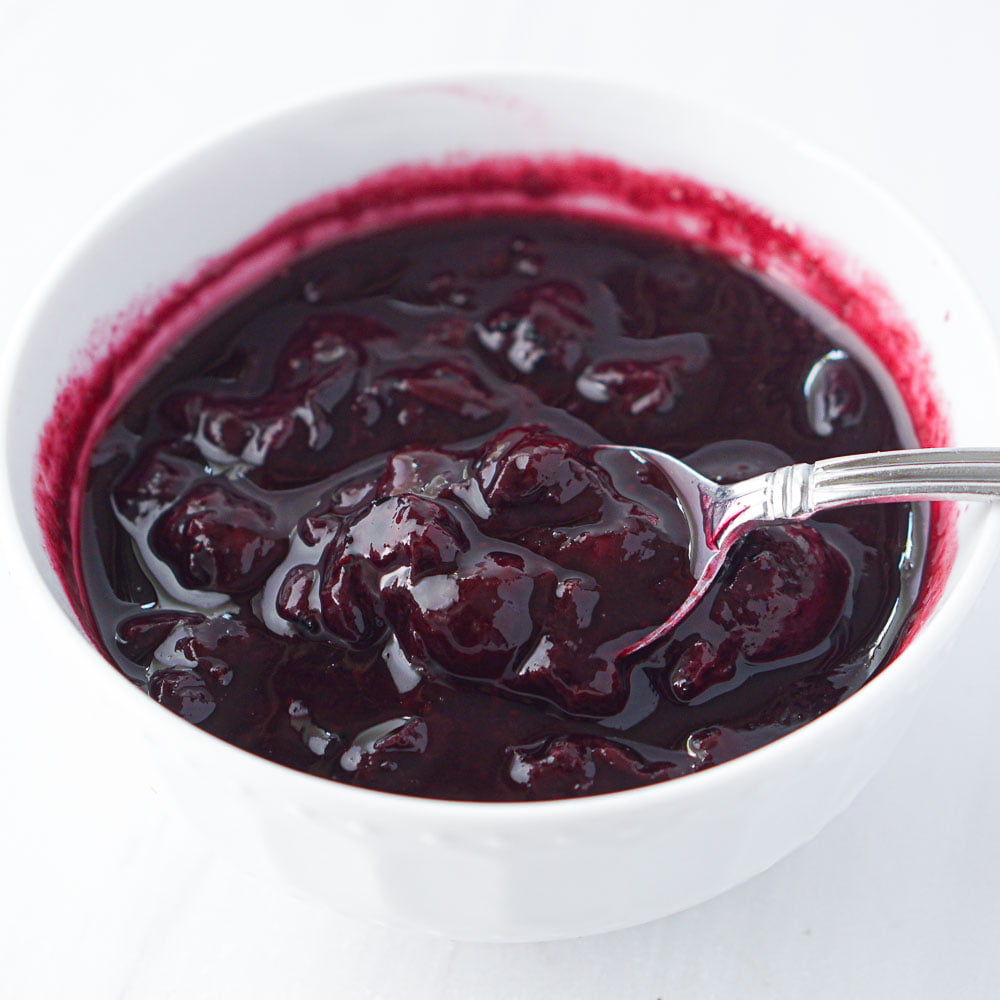 closeup of a white bowl with keto blueberry sauce and a spoon