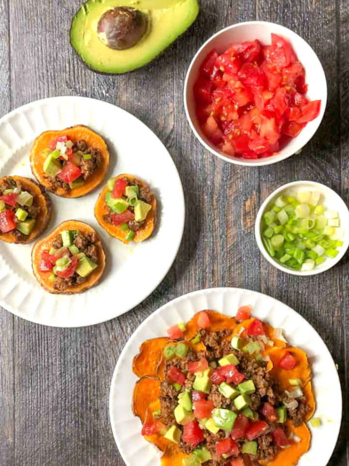 two white plates with sweet potato paleo nachos done two ways plus half an avocado and bowl of tomatoes 