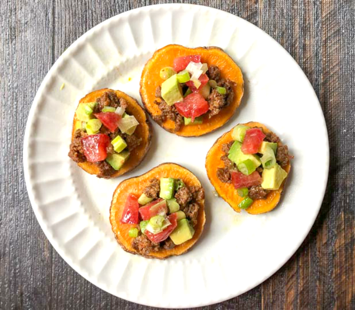 white plate with 4 sweet potato slices topped with nacho toppings