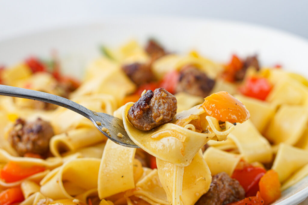 a forkful of wide pasta with peppers and sausage