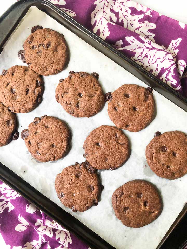 cookie sheet with baked cookies and a purple tea towel underneath