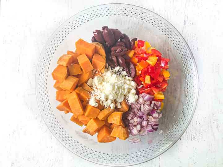 glass bowl with chopped sweet potatoes, feta, kalamata olives, yellow and red chopped peppers and chopped red onion