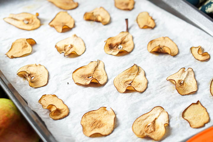 cookie sheet covered in parchment paper with thin dried apple chips on it