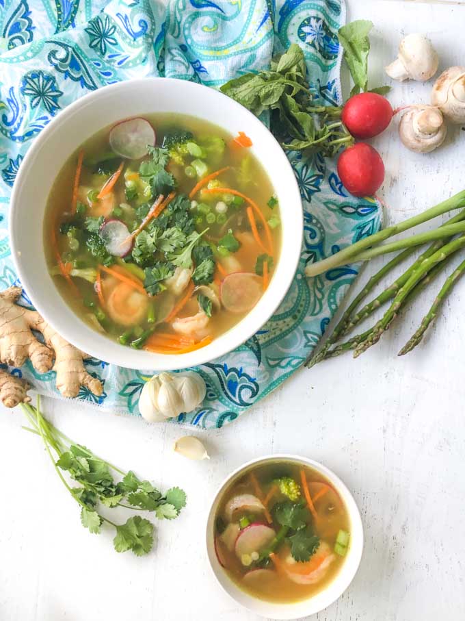 bowls of spring vegetable soups with blue towel and raw spring vegetables 