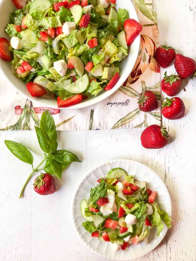 white bowl and plate full of strawberry caprese salad and fresh basil and strawberries on the side