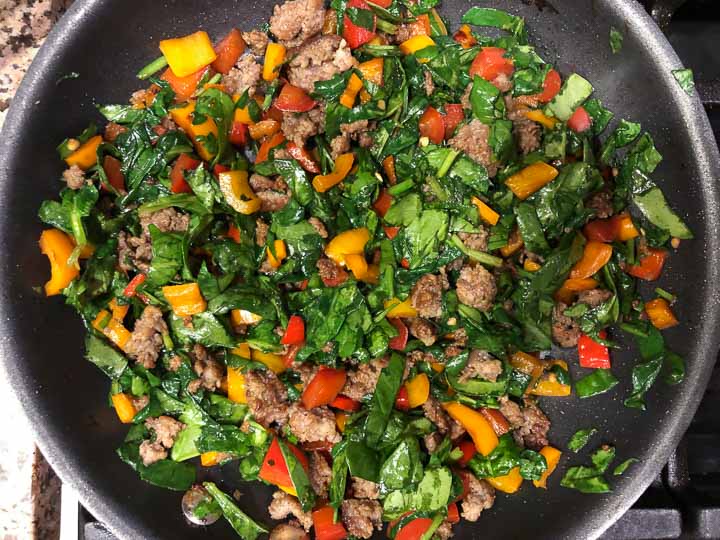 Skillet with sautéed sausage, peppers and spinach.