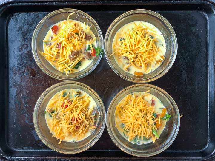 Baking sheet with 4 glass custard cups with omelets ready to bake.