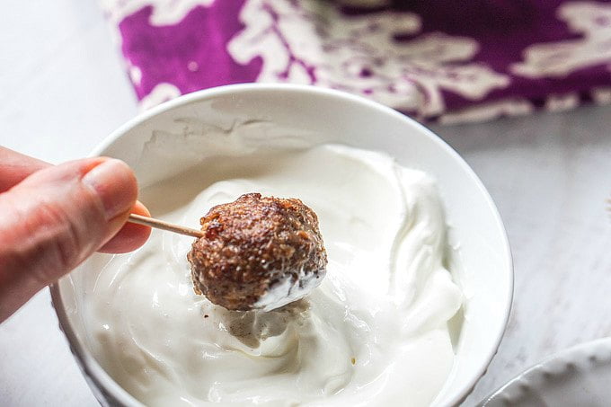 A bowl of yogurt and a toothpick with a meatball on it.