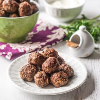 Photo of a white plate of middle eastern meatballs with a green bowl in background.