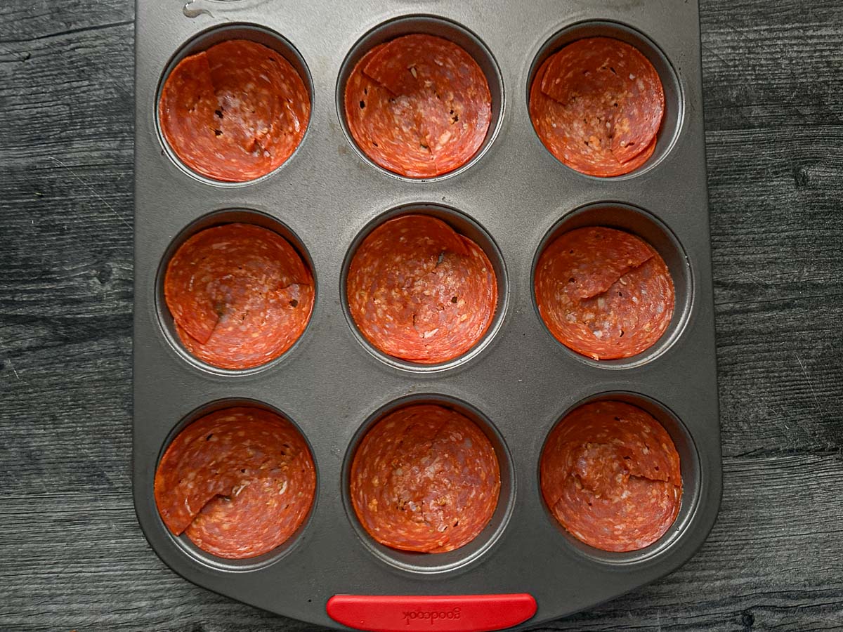 Muffin tin with the uncooked pieces of pepperoni.