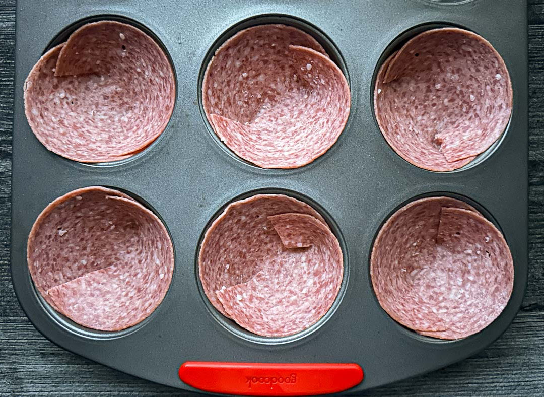 Muffin tin with pieces of salami ready to bake.