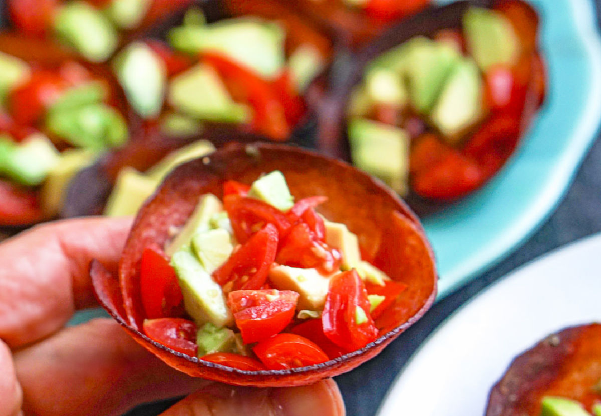 Closeup of a hand holding one of the low carb lunchmeat cups filled with avocados and tomatoes.