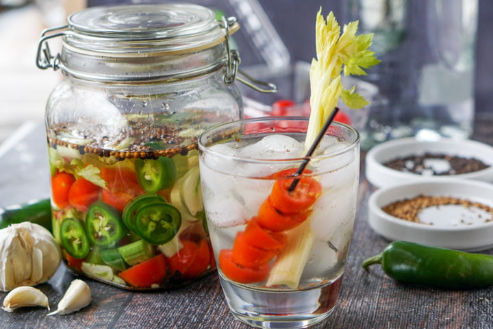 jar with Bloody Mary infused vodka in a jar and a drink with tomatoes and celery stalk