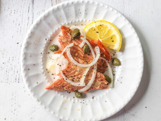 white plate with serving of smoked salmon with capers, onions and lemon