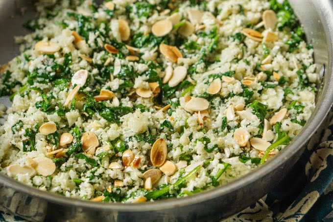 closeup of saute pan with spinach cauliflower rice with roasted almond slices on top
