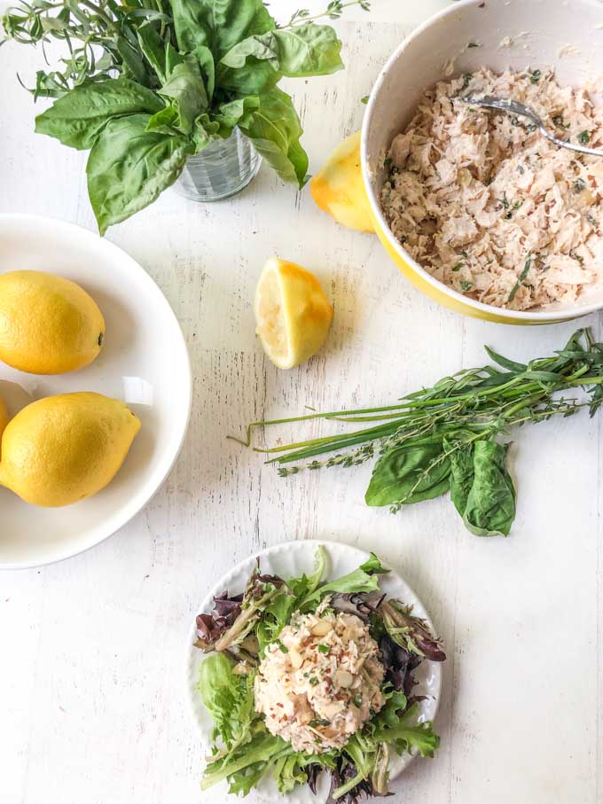 aerial view of plate of chicken salad with a bowl of lemons and fresh herbs