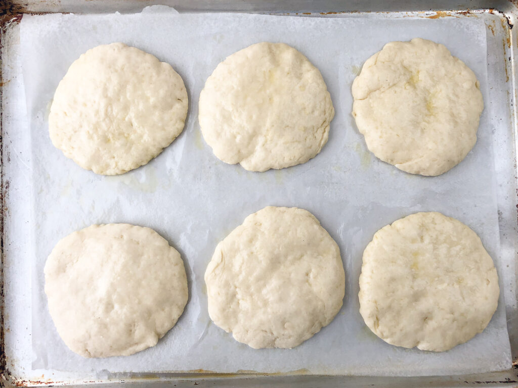 baking sheet covered in parchment paper with 6 mini precooked pizza crusts