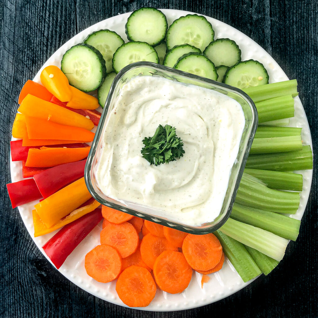 white plate with cut vegetables and a square glass bowl with dip using cottage cheese