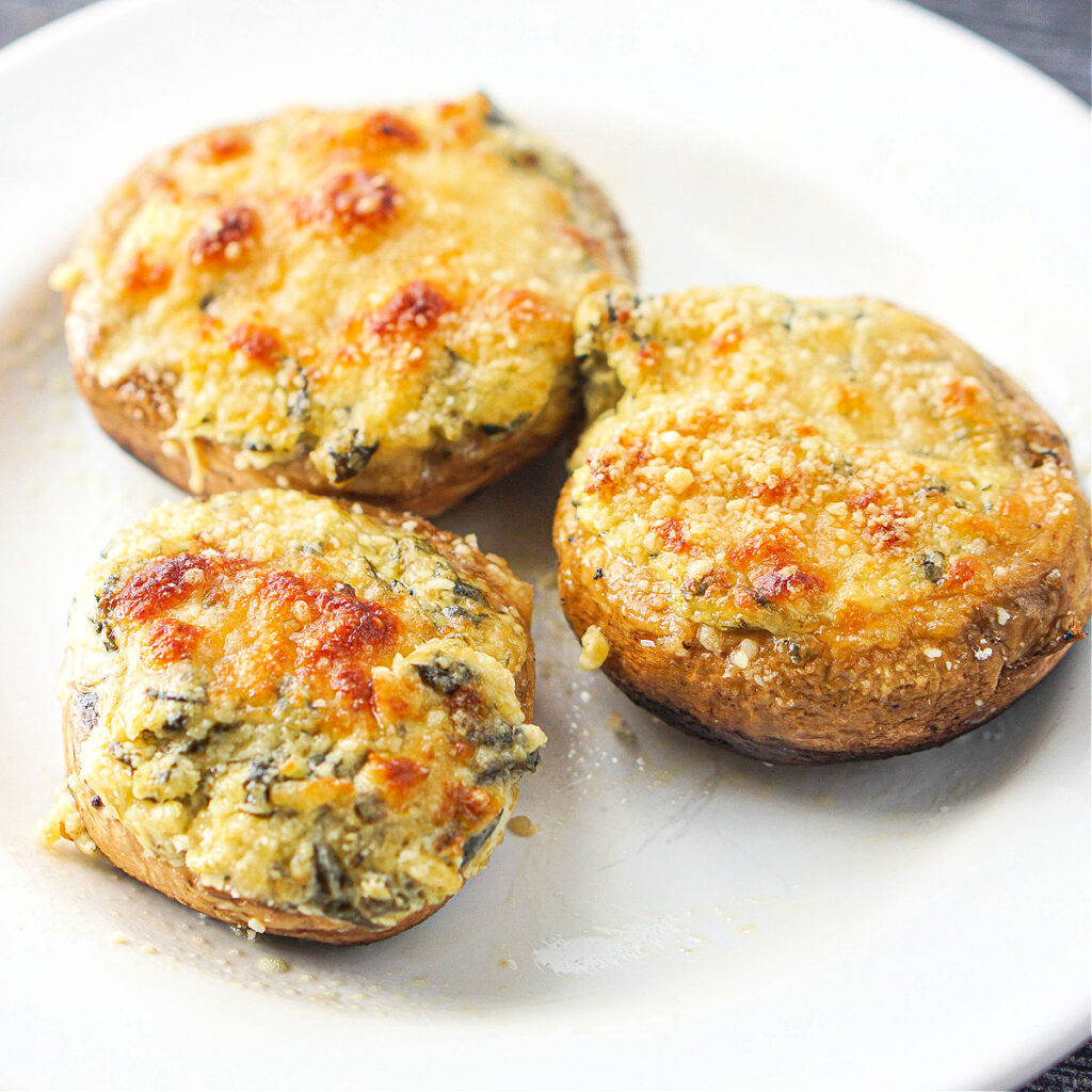 3 spinach and artichoke keto stuffed mushrooms on a white plate