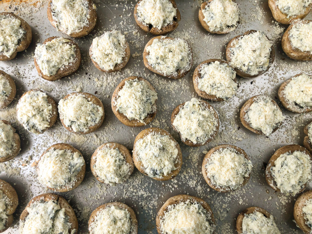 baking sheet with mushrooms stuffed  with  dip and topped with parmesan cheese