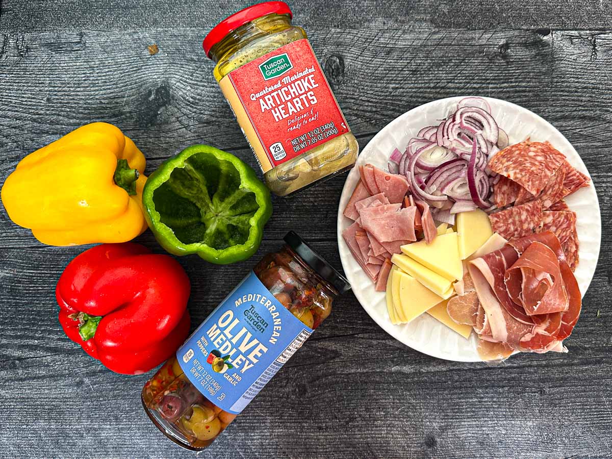 Recipe ingredients - assorted meats and cheeses, red onion slices, assort olives, artichoke hearts and fresh raw peppers.