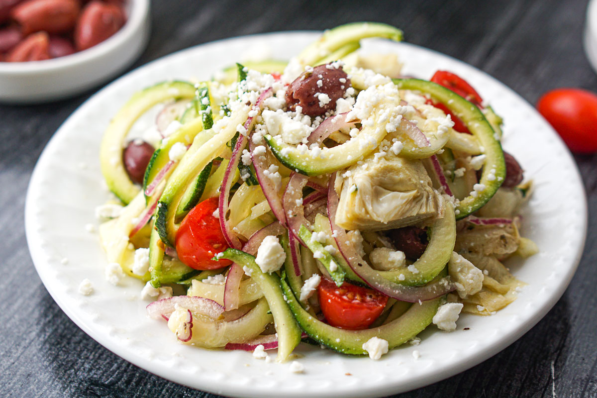 closeup of a white plate with zucchini noodle Greek salad