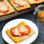 closeup of a pan of fresh tomato tarts with melted parmesan cheese and text