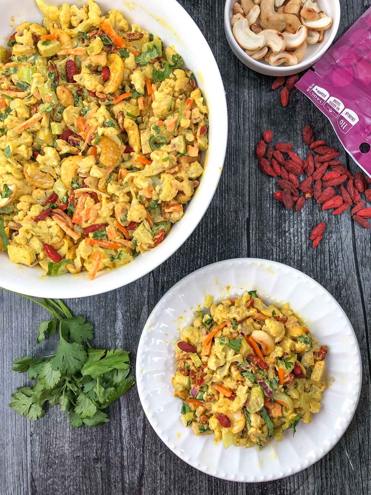 aerial view of white bowl and plate with curry cashew and cauliflower salad and fresh cilantro