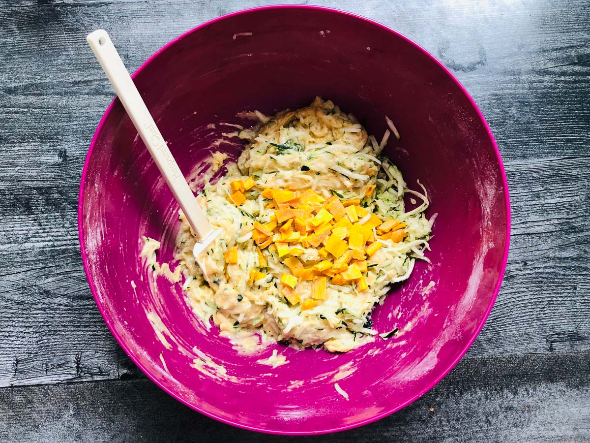 purple bowl with zucchini bread batter with chopped mangos