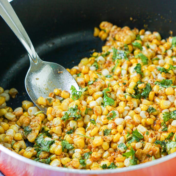 closeup of an orange pan with spicy Mexican corn with cilantro and a big spoon