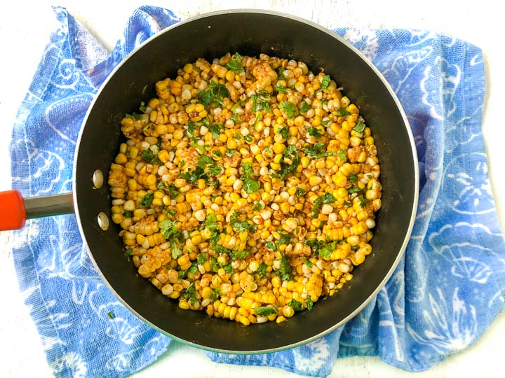 pan with the finished spicy Mexican corn with a bright blue towel underneath