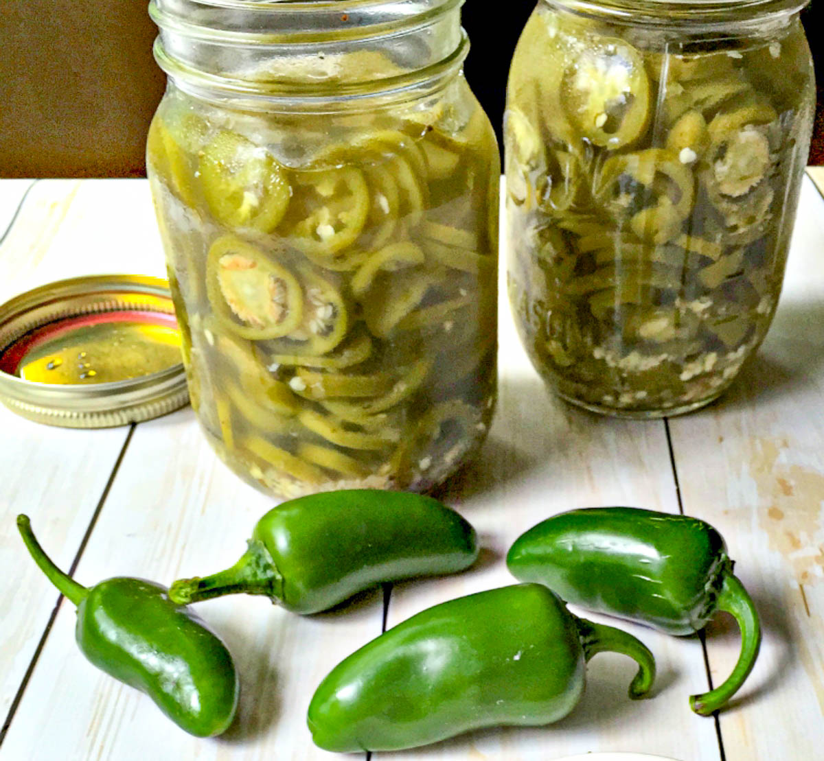 2 jars of homemade pickled jalapeno peppers and a few raw peppers in front of them