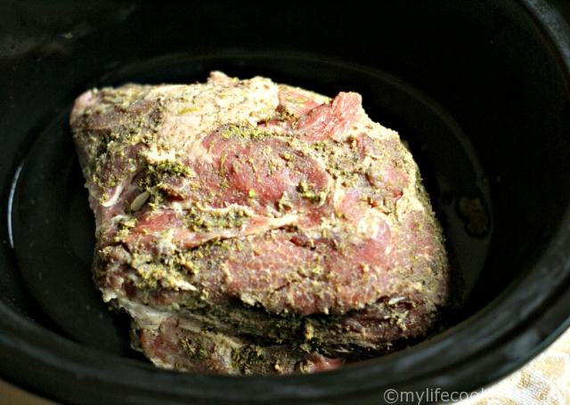 raw garlic pulled pork roast ready to go in a black slow cooker crock