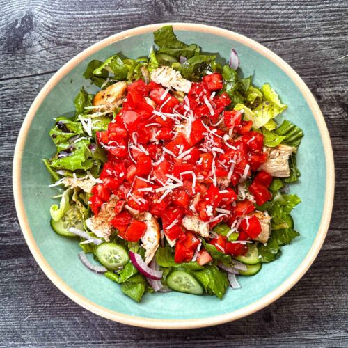 Aerial view of a aqua bowl with a high protein bruschetta salad with chicken.