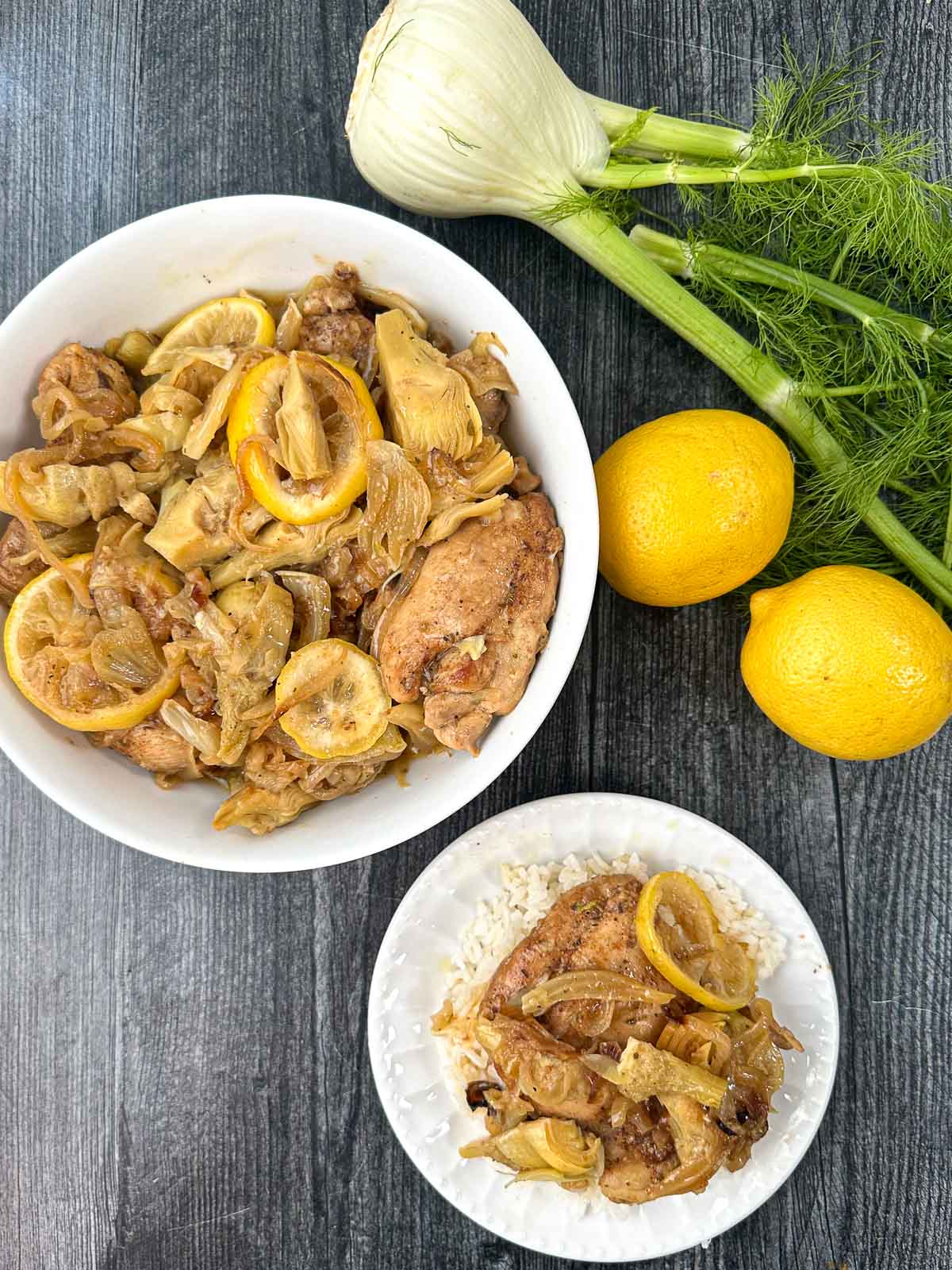 aerial view of white bowl and plate with a serving of fennel chicken with artichokes and a fresh fennel bulb and lemons