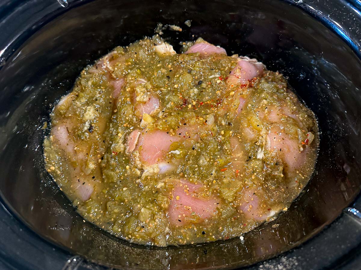 crockpot with raw chicken and green salsa poured over top